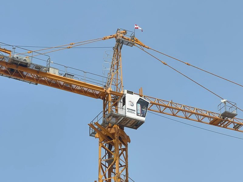 The top of a tower crane with its jib and cab against a pale blue sky