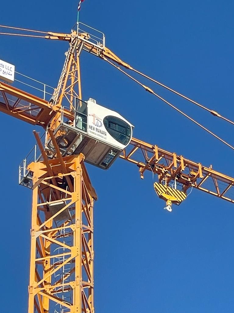 Close-up of the cab and jib of a yellow tower crane against a blue sky